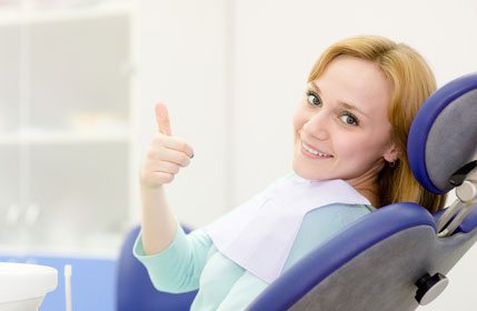A woman in a dental chair giving a thumbs up
