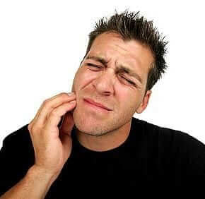 A man holding the side of his mouth from pain, in need of an emergency dentist